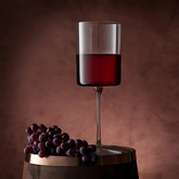 Monarch Stem Wine Glass — Pack of 6 featuring a tall refined design with red wine and grapes on a wooden barrel.