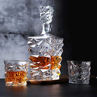 Crystal whiskey decanter set with two matching glasses on a dark surface