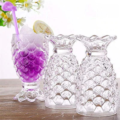 Pineapple-shaped clear glass tumblers with textured design on a wooden table, one filled with a colorful drink and ice.