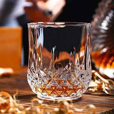 Crystal whiskey glass with amber liquid on wooden bar top, elegant barware design
