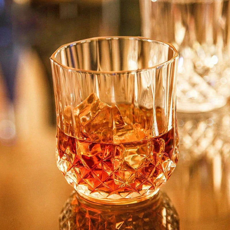 Crystal whiskey glass with amber drink and ice on a reflective bar surface