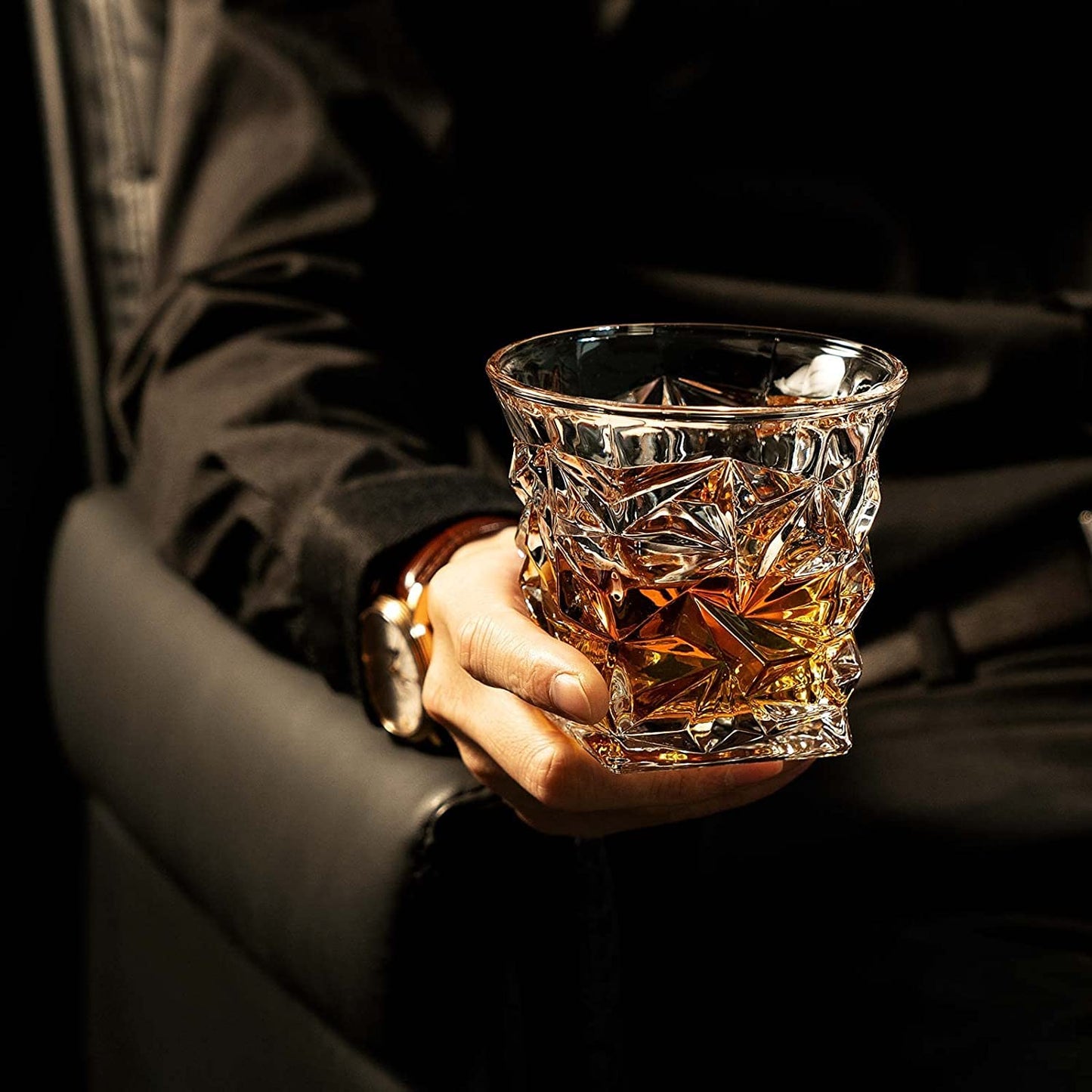 Hand holding a crystal whiskey glass with amber liquor in an elegant bar setting