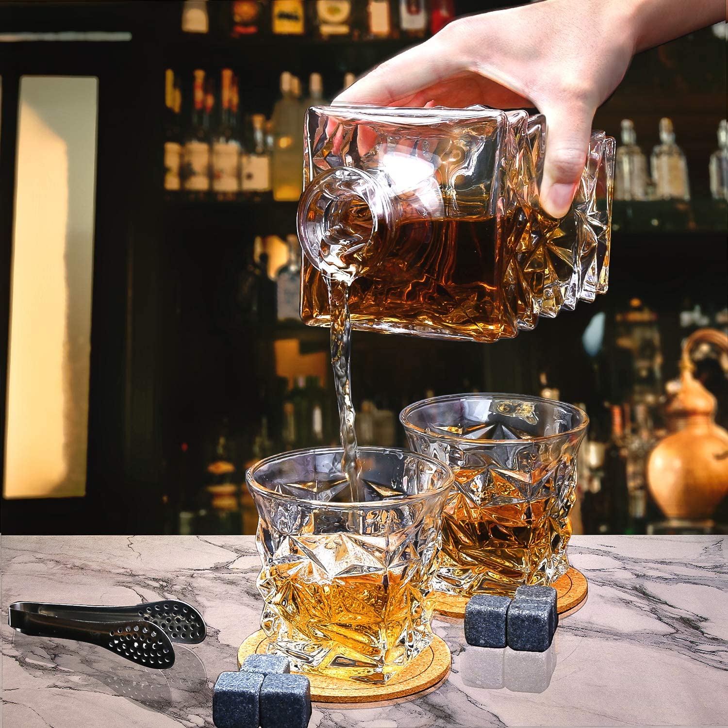 Crystal whiskey decanter pouring into two whiskey glasses on marble bar with whiskey stones