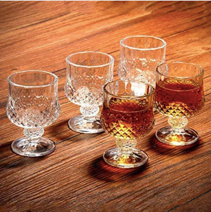 Set of five vintage-style whiskey glasses on wood surface, two filled with amber liquor.