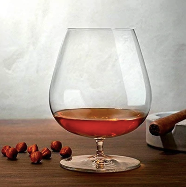 Crystal brandy glass with amber liquor, nuts, and cigar on wooden bar table
