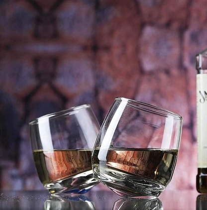 Two whiskey glasses with brown liquor on a reflective surface, rustic brick background