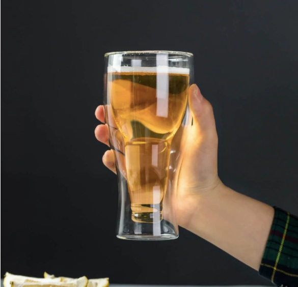 Hand holding a double-walled beer glass filled with light beer against a dark background